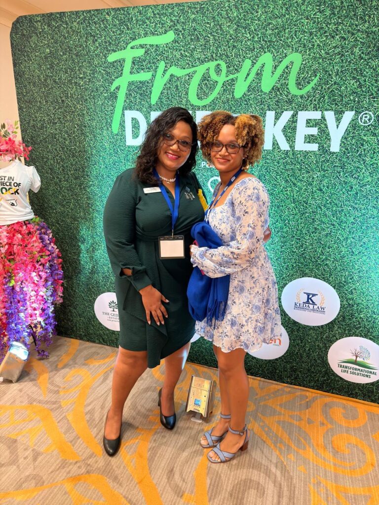 Two attendees at the From Deed to Key backdrop